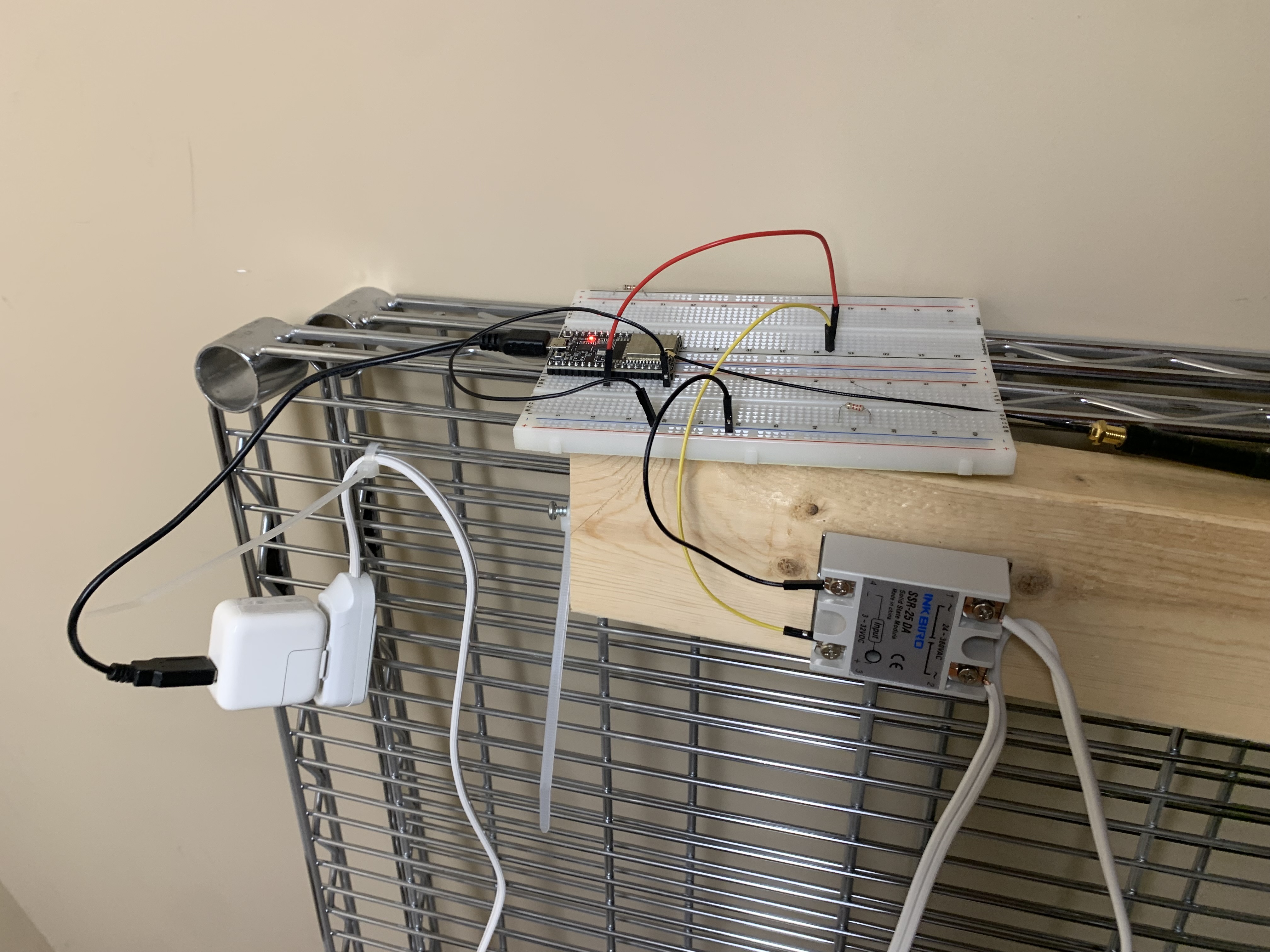 An ESP32 on a breadboard wired to an INKBIRD SSR-25 DA solid-state relay, mounted on a wood offcut and zip-tied to a wire shelf, powering a shop vac.